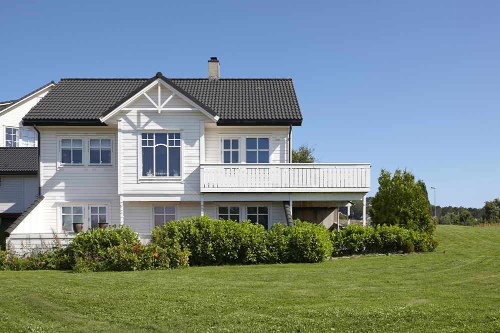 Ett traditionellt vitt trähus en solig sommardag mot en klarblå himmel och grön gräsmatta.