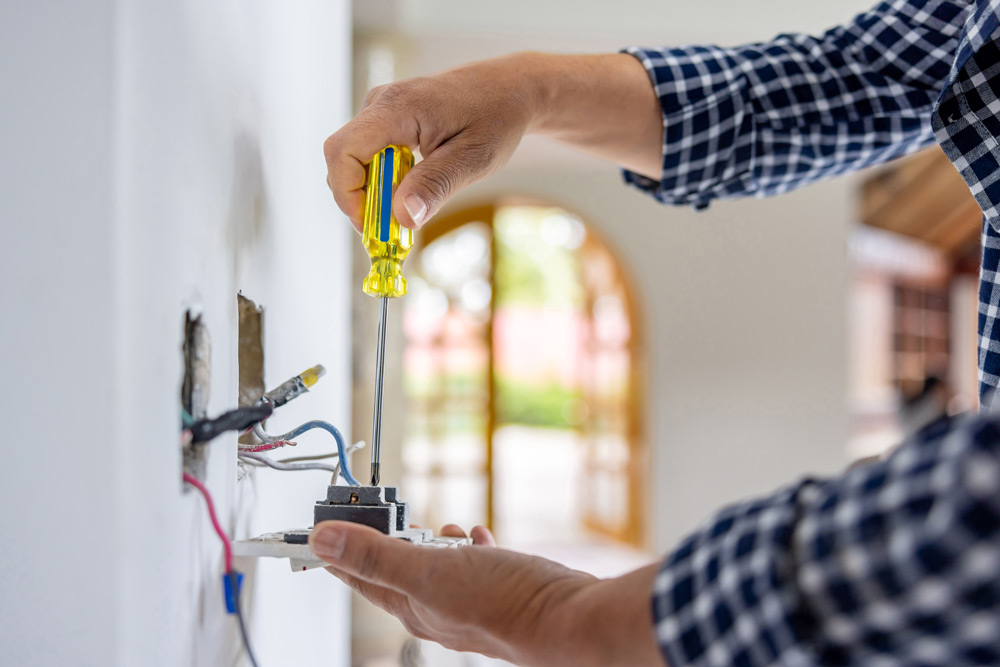 En elektriker i rutigt skjorta arbetar noggrant med installation av ett eluttag under husrenovering.