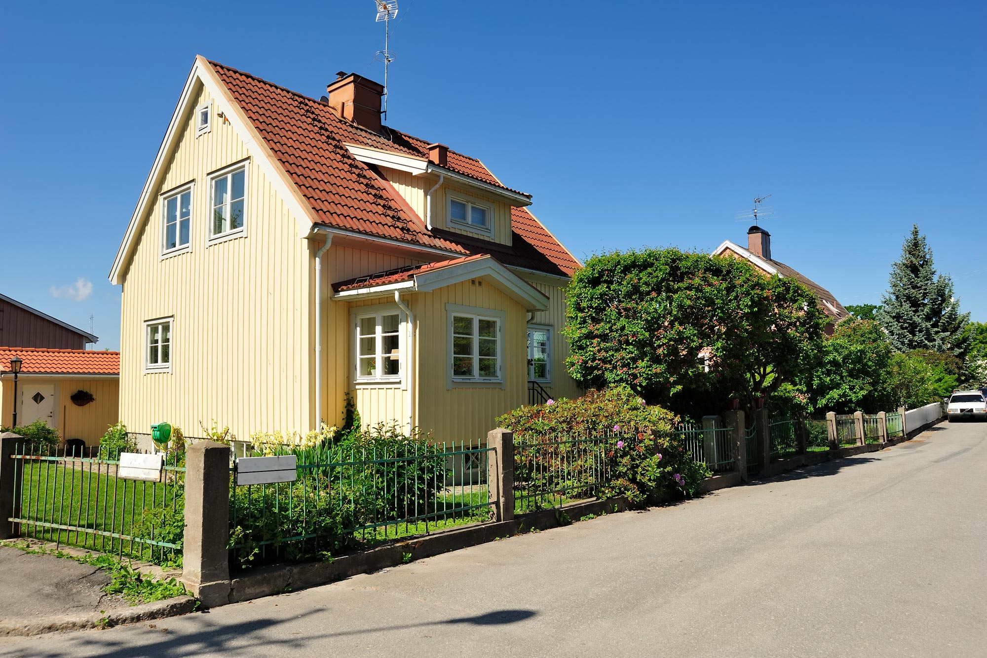 Ett charmigt gult trähus i traditionell skandinavisk stil med röda tegelplattor på taket och vita fönsterkarmar