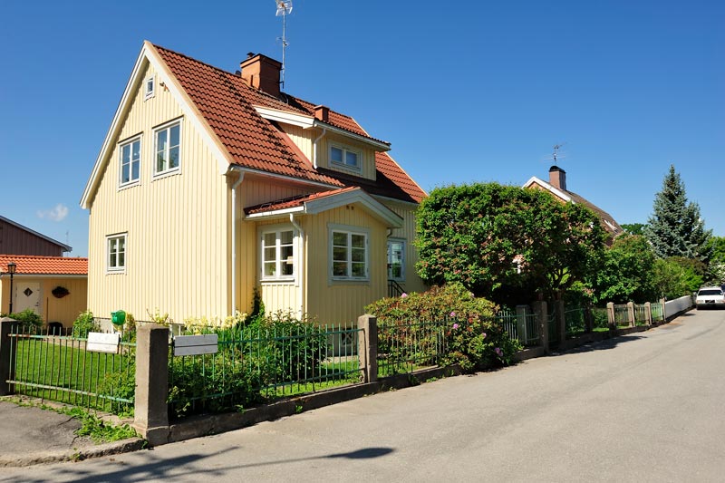 Ett charmigt gult trähus i traditionell skandinavisk stil med röda tegelplattor på taket och vita fönsterkarmar