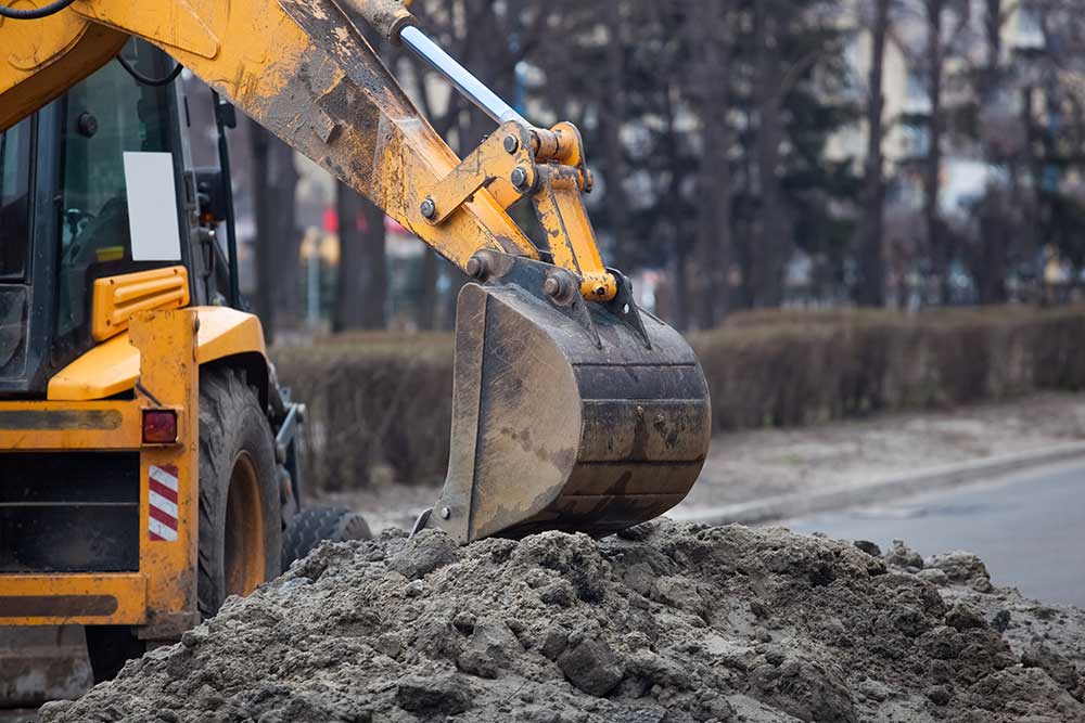 Gul grävmaskin som skopar upp sand