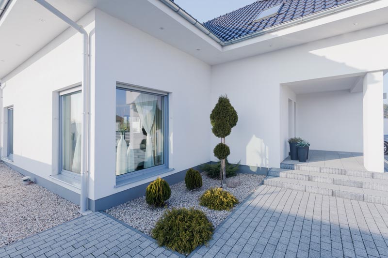 Exteriör av ett nybyggt modernt skandinaviskt enplanshus i vitt med stora fönster och diskret grå sockelbeklädnad